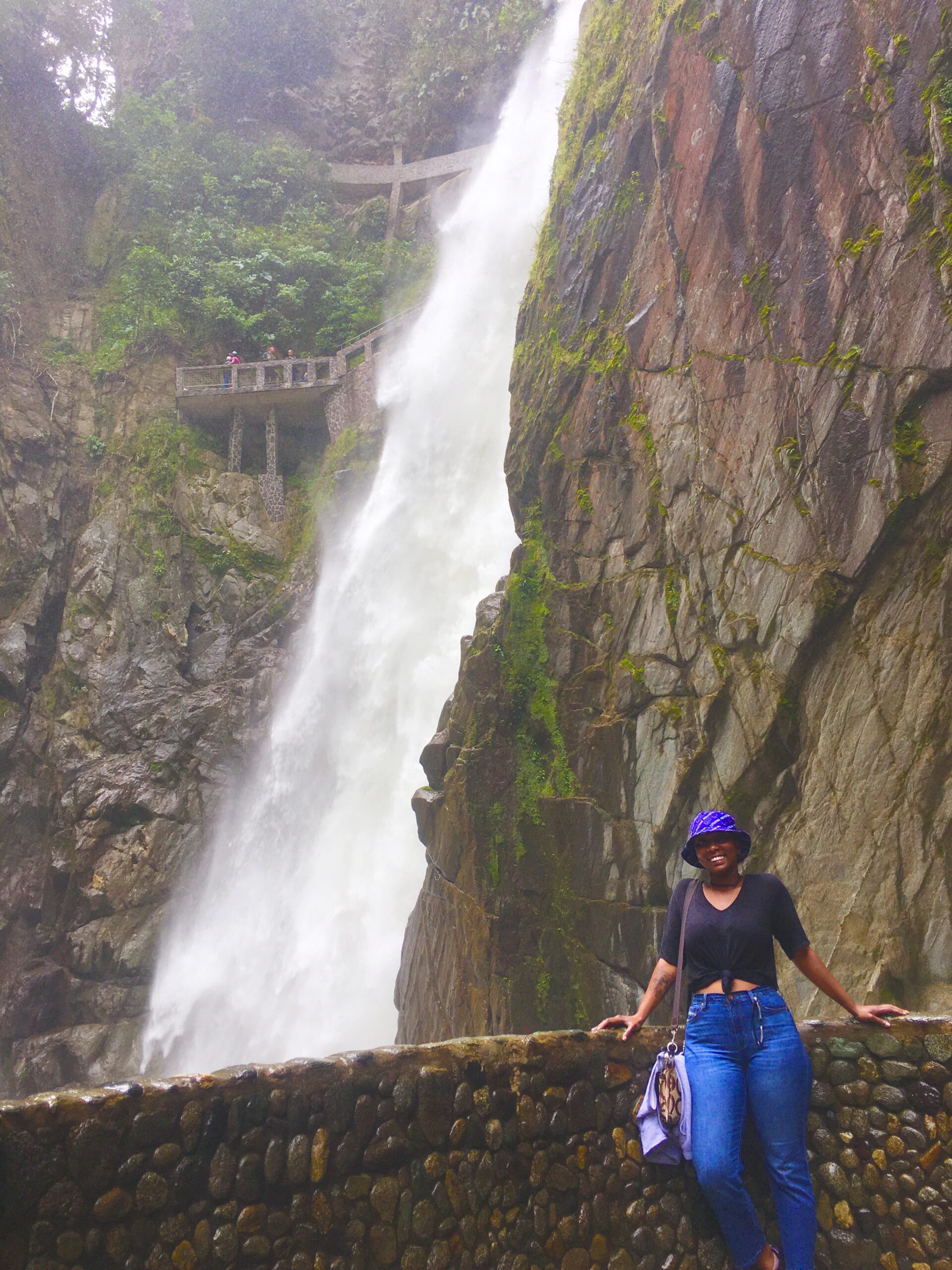 another image of Tina Williams. She is wearing casual clothes and standing in front of a large waterfall in Ecuador.
